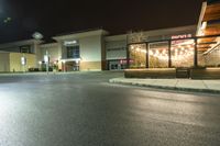 this is a parking lot at night with lights shining on the building and sidewalk in front of it