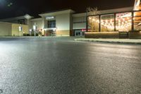 this is a parking lot at night with lights shining on the building and sidewalk in front of it