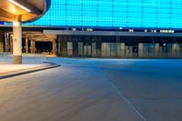 a paved street in front of a building with a blue glass wall above it at night