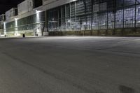 a big building with an empty parking lot at night time, on which cars are parked