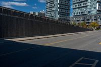 two tall buildings in a city, one behind the fence is a large street with yellow lines