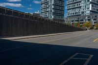 two tall buildings in a city, one behind the fence is a large street with yellow lines