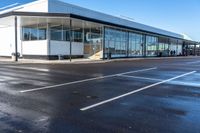 an empty parking lot with lots of windows next to a white building with a large roof