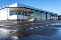 an empty parking lot with lots of windows next to a white building with a large roof