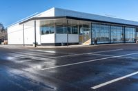 an empty parking lot with lots of windows next to a white building with a large roof