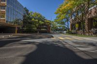 two tall buildings on both sides of a tree lined road with parked cars on it