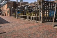 a brick sidewalk near buildings with a fence and tree in the center of it with a building in the background