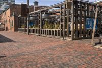 a brick sidewalk near buildings with a fence and tree in the center of it with a building in the background