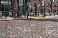 a brick street is shown with a large brick building in the background with a man walking in front