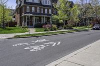 a paved city street with houses behind the curb with an arrow on the sidewalk and bike lanes