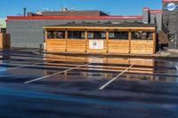 the car park with a wooden shelter is reflected in the wet street and parking lot