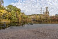 a brick walkway with benches near water and trees in the background against a bright blue sky