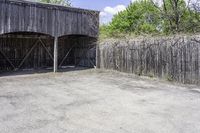 the view from behind the garage looking back at the inside of a barn with an outside entrance and grass, a fence, and trees behind which stands behind them are several gates