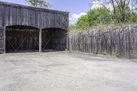 the view from behind the garage looking back at the inside of a barn with an outside entrance and grass, a fence, and trees behind which stands behind them are several gates