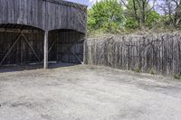 the view from behind the garage looking back at the inside of a barn with an outside entrance and grass, a fence, and trees behind which stands behind them are several gates