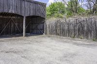 the view from behind the garage looking back at the inside of a barn with an outside entrance and grass, a fence, and trees behind which stands behind them are several gates