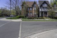 two houses in a residential area with one large building on the other side and trees in the street