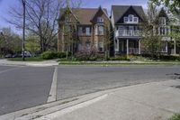 two houses in a residential area with one large building on the other side and trees in the street