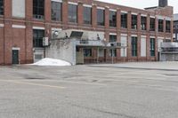 the empty parking lot has only snow on the ground in front of an old brick factory