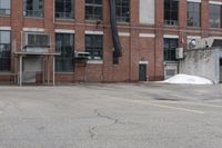 the empty parking lot has only snow on the ground in front of an old brick factory