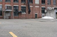 the empty parking lot has only snow on the ground in front of an old brick factory