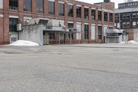 the empty parking lot has only snow on the ground in front of an old brick factory