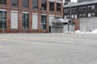 the empty parking lot has only snow on the ground in front of an old brick factory