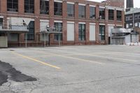 the empty parking lot has only snow on the ground in front of an old brick factory