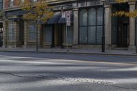 the empty street has cars on it and trees on either side of the road with buildings