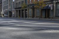 the empty street has cars on it and trees on either side of the road with buildings