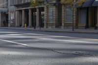 the empty street has cars on it and trees on either side of the road with buildings