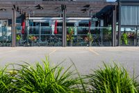 an empty building with red flags hanging on the front and outside of it and there are large green plants in the foreground