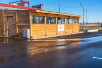 a wooden shop front with a red roof in the middle of the street and it's water reflecting on the road