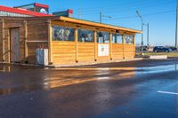 a wooden shop front with a red roof in the middle of the street and it's water reflecting on the road