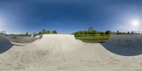 a bowl shaped skate board course is shown in a fish eye lens image against a sunny blue sky