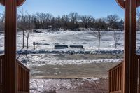 looking out into a large open gated park area in winter time with lots of snow on the ground