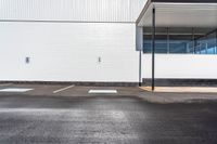 a parking lot with white walls and parking spaces in front of it and a light post outside