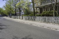 a street is lined with concrete fences and trees and buildings are behind it on both sides of the road