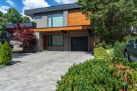 an elegant modern two story home with stone paving in the foreground and trees around it