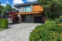 an elegant modern two story home with stone paving in the foreground and trees around it