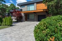 an elegant modern two story home with stone paving in the foreground and trees around it