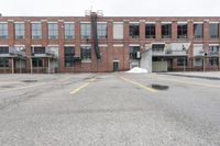 the empty parking lot has only snow on the ground in front of an old brick factory