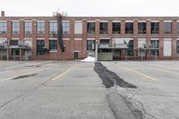 the empty parking lot has only snow on the ground in front of an old brick factory