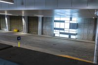 the empty parking garage has some concrete walls and signs on the wall, and a yellow garbage can in front of it