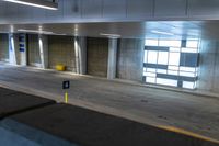 the empty parking garage has some concrete walls and signs on the wall, and a yellow garbage can in front of it