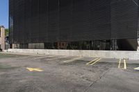 a parking lot in front of a black building with many windows and three yellow arrows