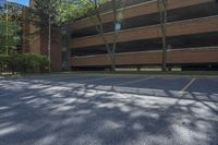 parking lot with parking garage, tree, and building in background and sunlight on street