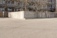 an empty parking lot with trees in the background in front of an apartment building with no roof