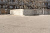 an empty parking lot with trees in the background in front of an apartment building with no roof