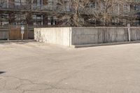 an empty parking lot with trees in the background in front of an apartment building with no roof